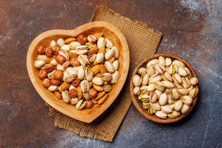 A vibrant mix of various nuts, including almonds, walnuts, hazelnuts, cashews, and pistachios, displayed in an heart shaped bowl, perfect for healthy snacking or culinary inspirationの写真素材