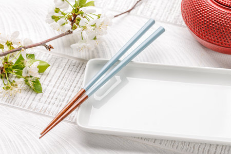 Empty plate on table adorned with cherry blossom branch and chopsticks, epitomizing Japanese food culture, providing ample copy spaceの写真素材