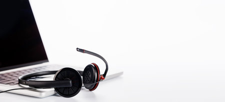 A sleek headset resting on a laptop, set against a bright white background with ample copy space. The high-key lighting emphasizes a clean and professional aesthetic, ideal for tech or work conceptsの写真素材