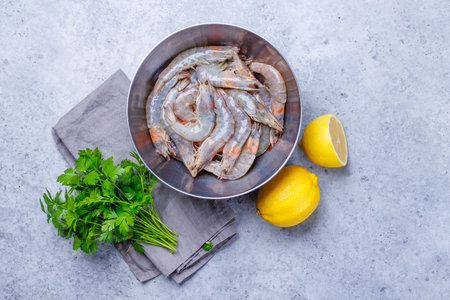 Fresh raw shrimps, accompanied by sprigs of fresh parsley and juicy lemon, ready for cooking. The vibrant colors of the ingredients create a visually appealing scene, perfect for a seafood preparationの写真素材