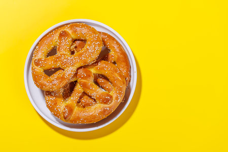 Pretzels scattered across a bright yellow background. The pretzels are golden-brown, perfectly baked, and sprinkled with coarse saltの写真素材