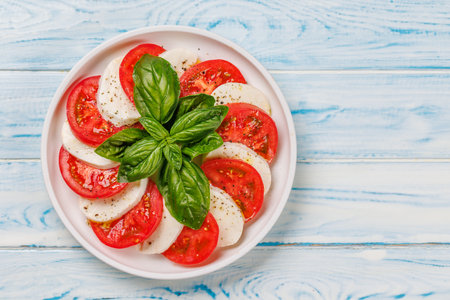 A vibrant and appetizing display of Caprese antipasti featuring slices of ripe garden tomatoes, fresh mozzarella, and aromatic basil leaves. Flat lay with copy spaceの写真素材