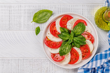 A vibrant and appetizing display of Caprese antipasti featuring slices of ripe garden tomatoes, fresh mozzarella, and aromatic basil leaves. Flat lay with copy spaceの写真素材