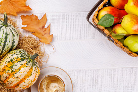 Autumn-themed food arrangement with coffee, pumpkins, pears, and autumn leaves on a table, creating a cozy seasonal atmosphere. Includes copy space for your contentの写真素材