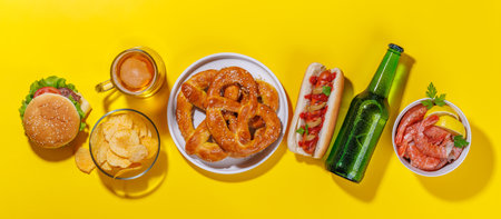 A vibrant photo showcasing a glass of beer surrounded by various snacks and fast food items, including a juicy cheeseburger, a classic hot dog, crispy potato chips, and salty pretzels, fresh shrimpsの写真素材