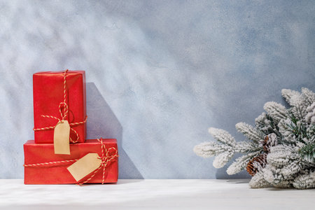Christmas template featuring gift boxes and snowy fir tree branches on a table with shadows and sun glares softly falling on the wall, creating a festive winter atmosphereの写真素材