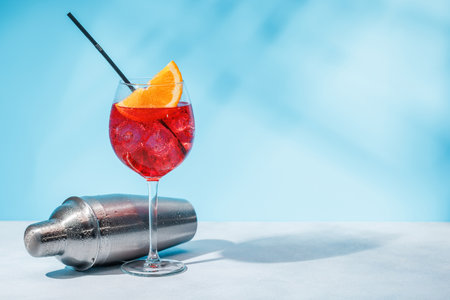 A cocktail and cocktail shaker arranged on a table against a light blue background, enhanced by sunny glares and playful shadowsの写真素材