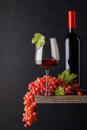 A glass and bottle of wine paired with grapes, set against a dark background, creating a rich and elegant ambianceの写真素材