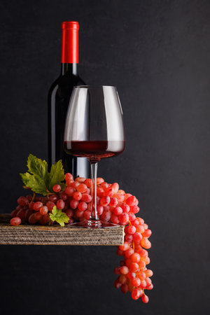 A glass and bottle of wine paired with grapes, set against a dark background, creating a rich and elegant ambianceの写真素材
