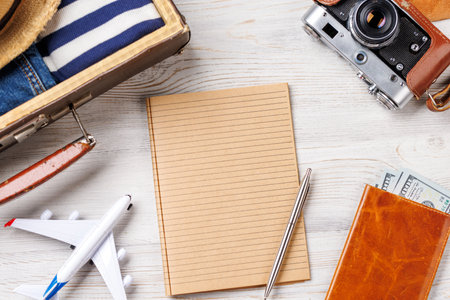 A travel bag with clothes, sun hat, flip flops, and a camera arranged on a wooden background, flat lay style, with blank notepad page for your textの写真素材