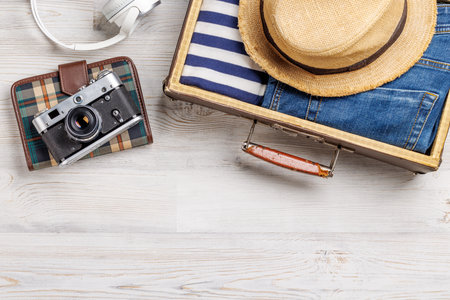 A travel bag with clothes, sun hat, flip flops, and a camera arranged on a wooden background, flat lay style, with copy space for your productの写真素材