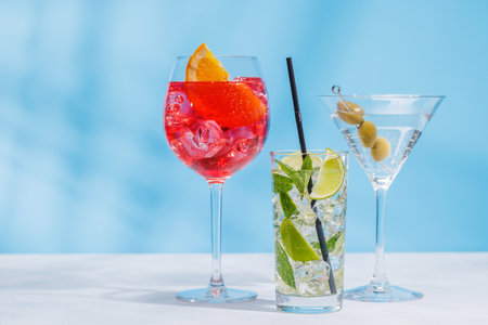 A variety of cocktails arranged on a table against a light blue background, enhanced by sunny glares and playful shadowsの写真素材