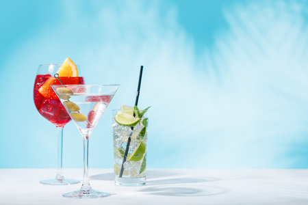 A variety of cocktails arranged on a table against a light blue background, enhanced by sunny glares and playful shadows, with copy spaceの写真素材