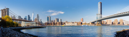 A sunny panoramic view of Manhattan framed between the Brooklyn and Manhattan bridges, showcasing iconic skyscrapers under a clear blue skyの写真素材