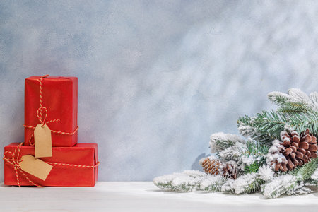 Christmas template featuring gift boxes and snowy fir tree branches on a table with shadows and sun glares softly falling on the wall, creating a festive winter atmosphereの写真素材