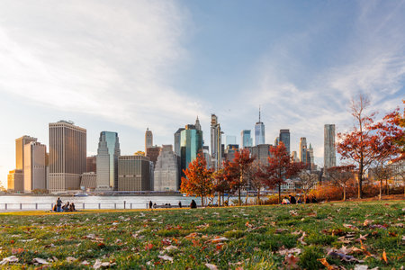The New York skyline during autumn sunset, with iconic skyscrapers framed by golden and orange foliageの写真素材
