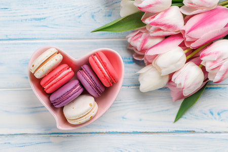 Pastel colorful tulips and vibrant macaroons fill a heart-shaped bowl, offering a delightful and charming scene perfect for celebrations or joyful momentsの写真素材