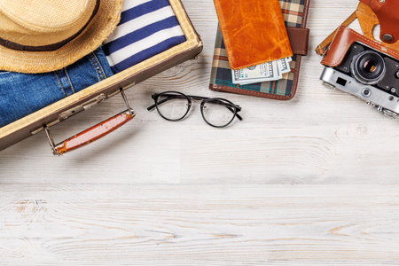 A travel bag with clothes, sun hat, flip flops, and a camera arranged on a wooden background, flat lay style, with copy space for your productの写真素材