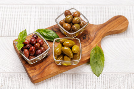 An assortment of various olives presented in glass bowls and olive oil, showing different colors, textures, and flavorsの写真素材