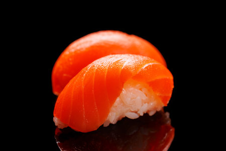 Salmon sushi beautifully arranged, featuring fresh ingredients and vibrant colors, on a clean black backgroundの写真素材
