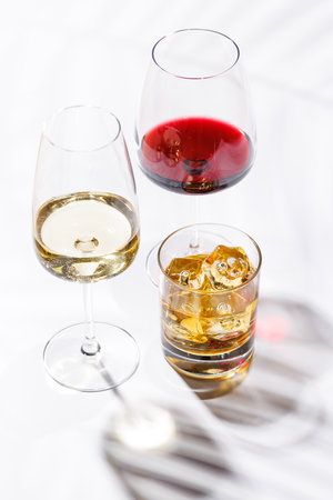 A refined composition of wine glasses filled with red and white wine, paired with a whiskey glass on a bright, minimalist background. A sophisticated display for connoisseurs of fine beveragesの写真素材