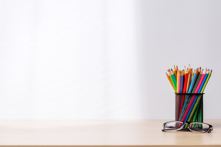 A desk organizer holding colorful pencils and eyeglasses placed on a table, showcasing a vibrant and organized workspace setup with copy spaceの写真素材