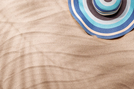 A tropical summer background featuring soft beach sand with delicate palm leaf shadows and a stylish sunhat, evoking a warm and relaxing seaside vibeの写真素材