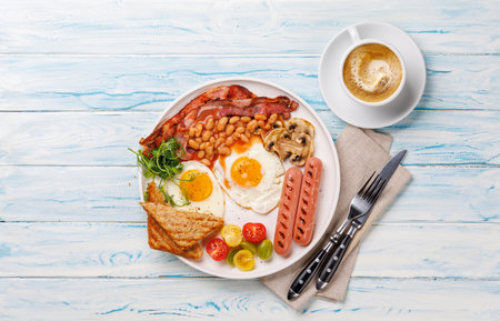 A classic breakfast plate featuring sunny-side-up eggs, crispy bacon, sausages, and fresh tomatoes,...