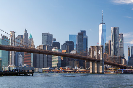 A stunning panoramic view of the iconic Brooklyn Bridge stretching gracefully towards Manhattan's skyline, capturing its timeless architectural beauty and urban charm under a clear skyの写真素材