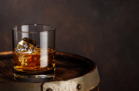 A classic whiskey glass filled with golden amber whiskey, placed on a wooden barrelの写真素材