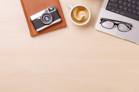 A clean and minimal desk setup featuring a laptop, camera and a coffee cup, providing a perfect workspace with ample copy space for design or textの写真素材
