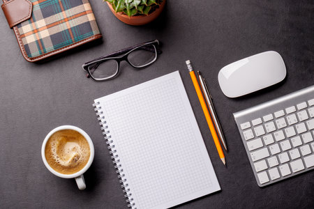 Top view of a dark leather office desk with blank notepad, supplies, and coffee cup. Elegant workspace setup with copy spaceの写真素材