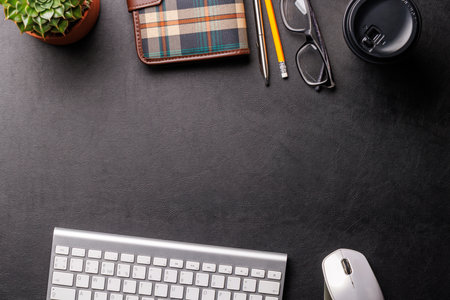 Top view of a dark leather office desk with potted plant, supplies, and coffee cup. Elegant workspace setup with copy spaceの写真素材