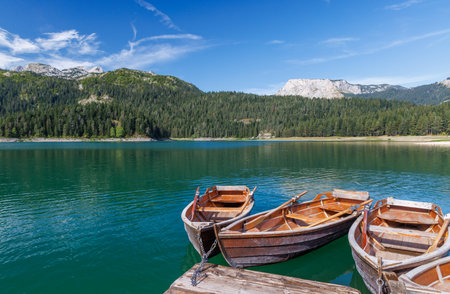 Scenic lake view with small boats floating gently, framed by distant mountains on the horizon under a clear skyの写真素材