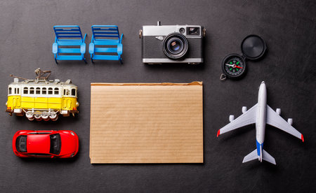 Creative flat lay of a travel-themed desk with notepad for plans, travel toys like airplane and tram, and accessories such as camera and compassの写真素材