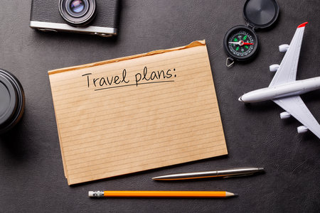 Creative flat lay of a travel-themed desk with notepad for plans, travel toys like airplane, and accessories such as camera and compassの写真素材