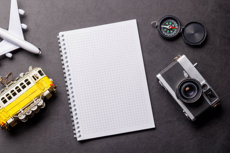 Creative flat lay of a travel-themed desk with notepad for plans, travel toys like airplane and tram, and accessories such as camera and compassの写真素材