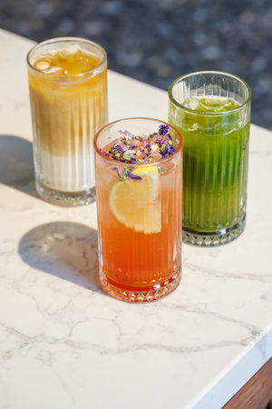 Assorted summer lemonades in glass jars with fresh fruits, ice, and colorful garnishesの写真素材