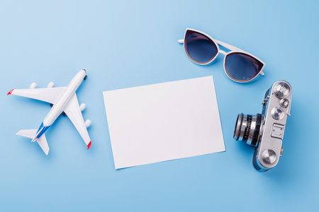 Travel-themed flat lay with blank photo card, camera, toy airplane, and sunglasses, arranged creatively on table with copy space for your ideasの写真素材