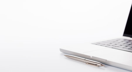 Closeup of an office table featuring a sleek laptop, a pen, and pencil on a clean white surface with ample copy space, presented in high-key lighting for a minimalistic and professional vibeの写真素材
