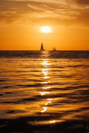 Sunset over the sea with sailing boats on the horizon under a colorful skyの写真素材