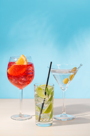 A variety of cocktails arranged on a table against a light blue background, enhanced by sunny glares and playful shadowsの写真素材