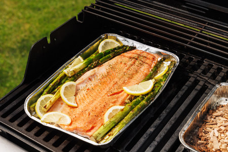 Grilled salmon fillets and asparagus sizzling on a barbecue grill with smoky char marksの写真素材