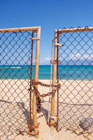 Beach entrance closed with a metal fence and lock in the foreground, sand and sea visible beyondの写真素材
