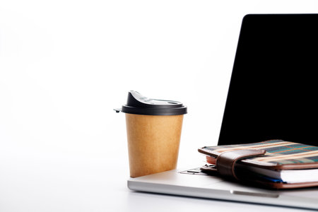 Closeup of an office table featuring a sleek laptop and a coffee cup on a clean white surface with ample copy space, presented in high-key lighting for a minimalistic and professional vibeの写真素材