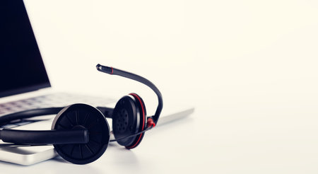 A sleek headset resting on a laptop, set against a bright white background with ample copy space. The high-key lighting emphasizes a clean and professional aesthetic, ideal for tech or work concepts. Tonedの写真素材