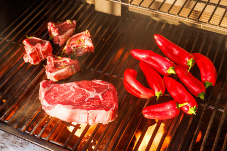 Juicy steaks and bell peppers sizzling on a grill with flames and smoke risingの写真素材