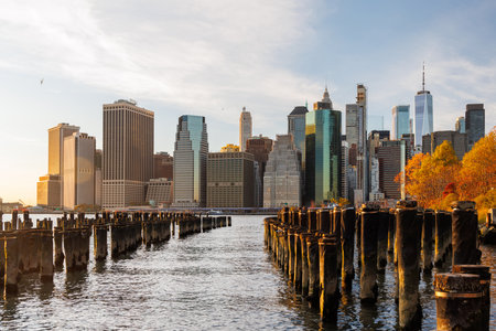 The New York Manhattan skyline during autumn, with iconic skyscrapers framed by golden and orange foliageの写真素材