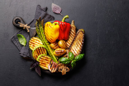 Assorted grilled vegetables including bell peppers, zucchini, eggplant, and asparagus arranged on a rustic wooden board, captured in a vibrant flat lay compositionの写真素材