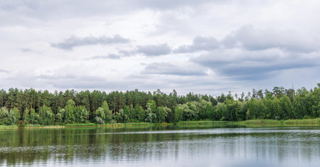 Scenic landscape with a calm lake surrounded by lush green forest under a moody skyの写真素材